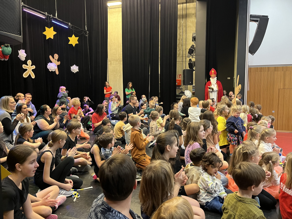 Auf der Bühne in der Mehrzweckhalle der Nendinger Donau-Hallen hören im sitzen ganz viele Kinder dem Nikolaus aufmerksam zu.