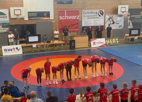 12 Rope-Skipping Mädels stehen in der Gruppe zusammen in Ihrer Auftrittskleidung in den Farben rot, weiß und schwarz mit zum Teil hochgehaltenen PomPoms in den Farben weiß und glitzernd.
